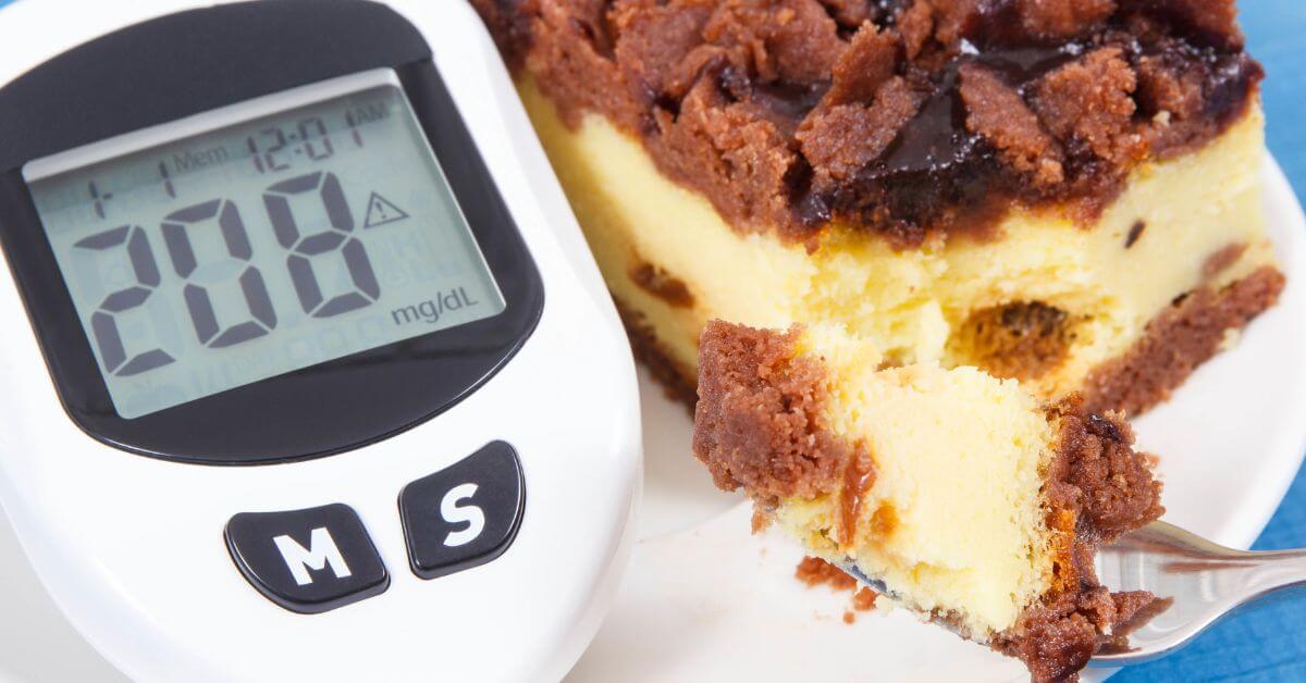 A blood glucose meter displaying 208 mg/dL is next to a piece of cake and a fork with a bite of cake on it.