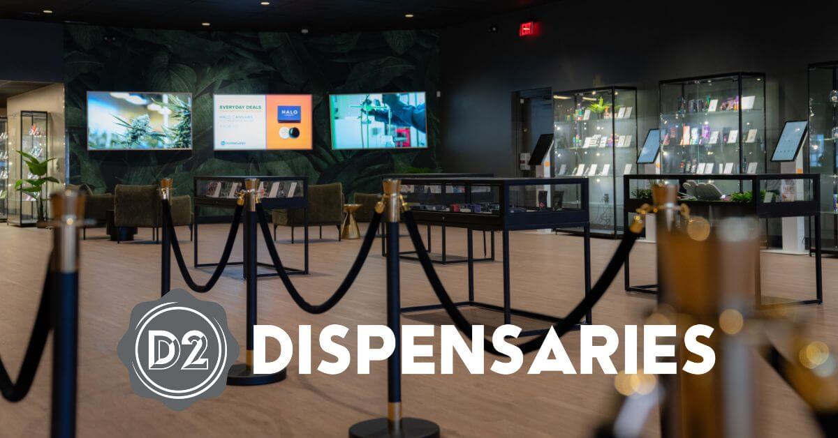 Modern dispensary interior with glass display cases, digital screens on the wall, and rope barriers separating walkways. "D2 DISPENSARIES" logo and text overlay on the image.
